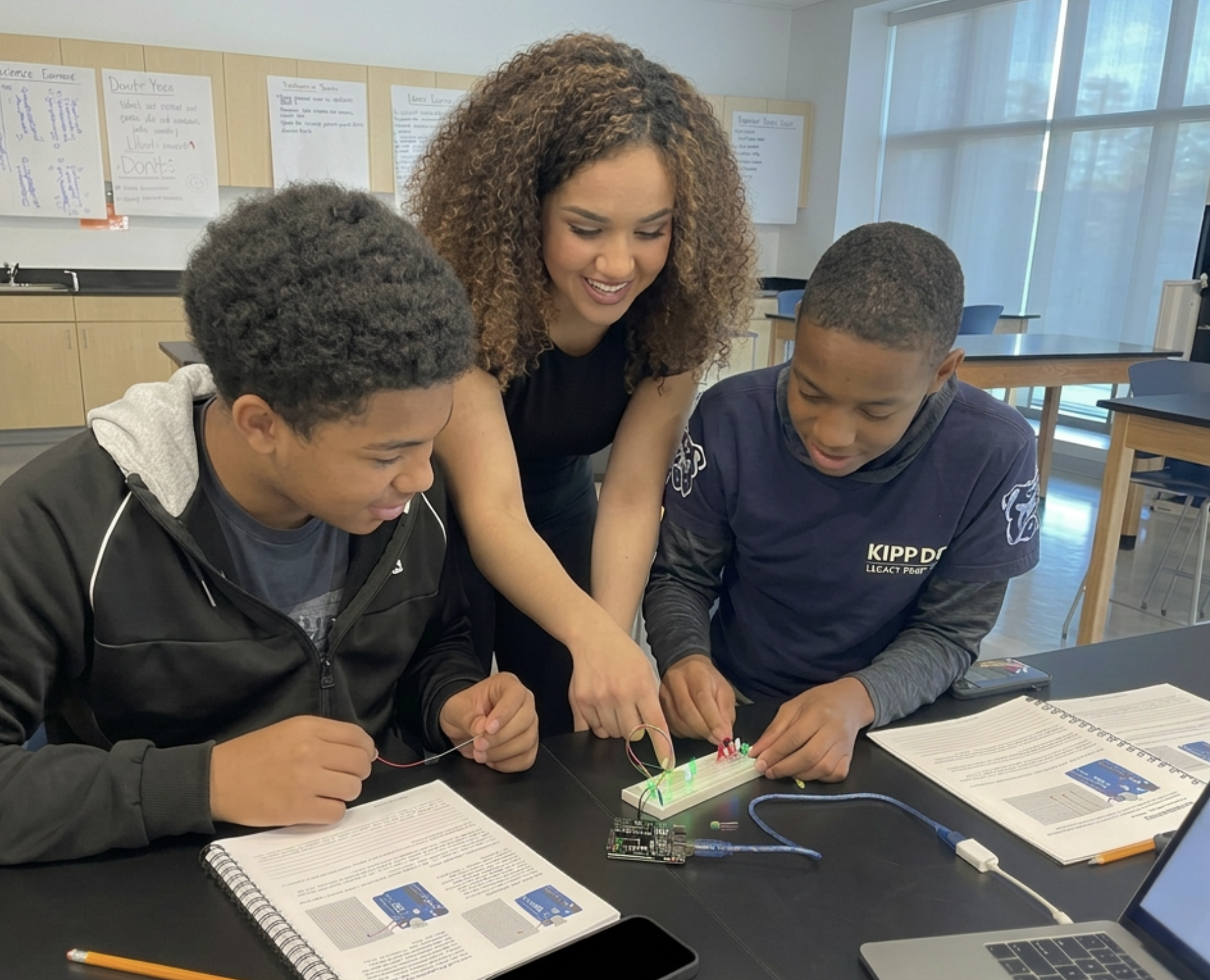 Maryam working with two students on a circuit board during an empowerment workshop